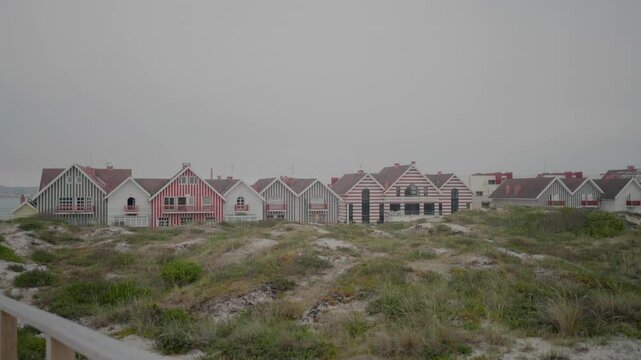 Colorful striped houses at Praia da Costa Nova in Aveiro, Portugal, with sand dunes in the foreground