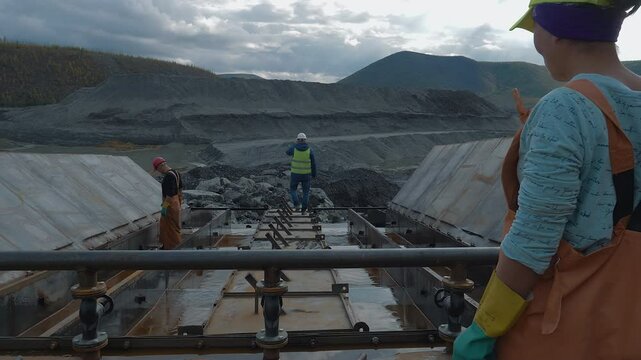 Multiple workers deal with the gold mining process at the industrial quarry. Industrial Labourers mining for gold. Industrial mining equipment looking for rich gold metal pieces in collected stones.