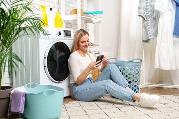 Woman Using Smartphone Near White Laundry Machine in Home Laundry Room