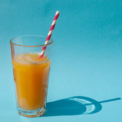 Glasses with orange or pumpkin juice and straw on a blue background with shadow from the sun