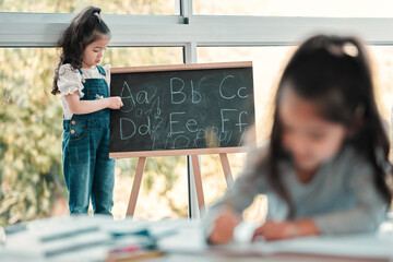 Little girl, blackboard and writing alphabet in classroom for education, literature or knowledge. ABC, childcare development and kids with foundation for literacy, grammar or language in kindergarten
