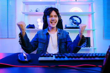 Portrait of Asian male gamer celebrating victory in front of the gaming table. Gamer winning an esports game with victory emotion. The player rejoices in victory in the competition.