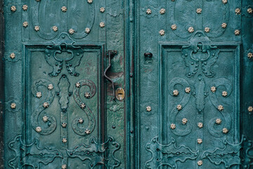 An old green metal door with an openwork ornate pattern. Vintage background closeup. Medieval forging technologies.