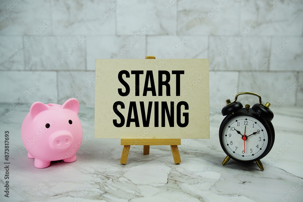 Poster start saving text written on paper card with piggy saving and alarm clock on marble background