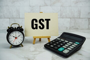 GST, goods and services tax text written on paper card with calculator and alarm clock on marble...