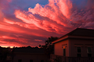 Dramatic sunset with vibrant pink and orange clouds over a silhouetted house, creating a serene and picturesque summer evening atmosphere
