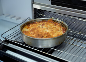 Close-up of authentic italian round lasagna baking in the oven, with melted cheese and crispy, golden edges.