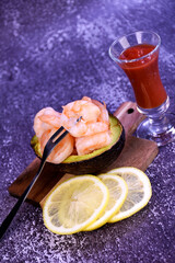 Shrimp in half an avacado on a wooden board with lemon slices and cocktail on a gray background