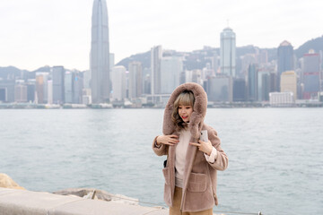 Young Hong Kong woman in her 20s wearing warm winter clothes, smiling in the sunset with high-rise...