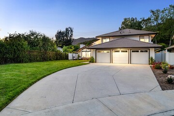 suburban house with a large driveway and well-maintained lawn at sunset