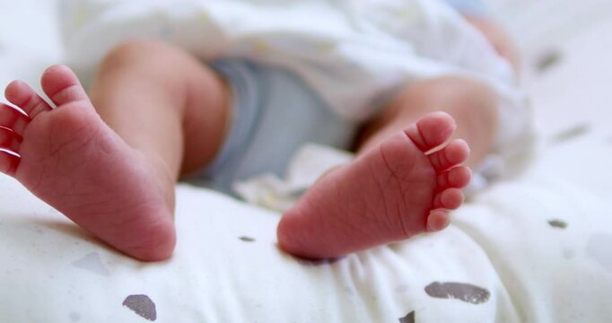 Close-up shot of the cute, tiny feet and toes of a newborn baby as she stretches and kicks while lying in her crib.