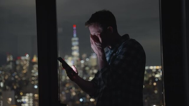Man or businessman holding smartphone reading and looking at screen at night with metropolitan city buildings in the background. Unhappy and disappointed or feeling bad. Texting and shaking his head