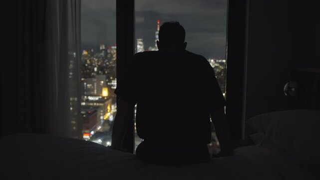 Man turning off the light in bed room. Lonely Guy sitting on hotel bed reaching to night lamp and turning it off. businessman after a long day of work going to sleep. Manhattan NY in the background.