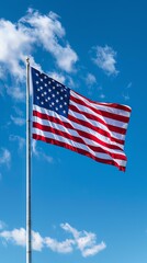 A large American flag is blowing in the wind against a blue sky with white clouds.
