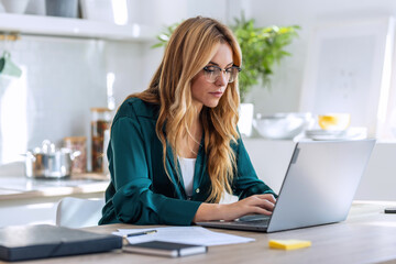 Pretty young woman working with laptop during morning coffee in the kitchen at home.