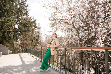 A woman is standing on a ledge with a cup of coffee in her hand. She is wearing sunglasses and a...
