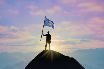 Waving flag of Kosovo at the top of a mountain summit against sunset or sunrise. Kosovo flag for...