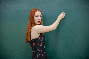 A woman with red hair stands in front of a green chalkboard