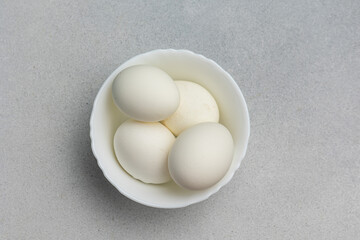 Boiled eggs in a white bowl on a gray background with copy space