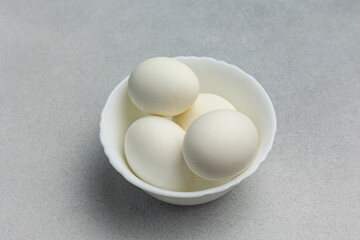 Boiled eggs in a white bowl on a gray background with copy space