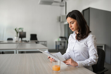 Young attractive brunette reading paper documents while sitting at her desk