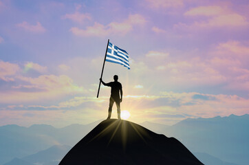 Waving flag of Greece at the top of a mountain summit against sunset or sunrise. Greece flag for Independence Day.