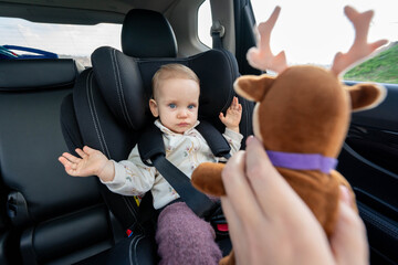 Mother trying to entertain baby in car seat with a toy