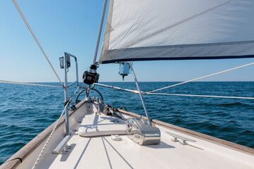Obraz premium White yacht sailing on a sunny summer day. Top down view from the deck to the bow, mast and headsail. Waves and water splashes. Clear blue sky. Gulf of Finland