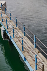 Old weathered concrete pier with rusting blue rail overlooking calm waters