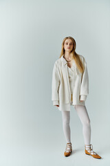 A stylish young woman stands in a studio, wearing an all-white outfit.