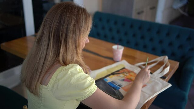 a  beautiful young artist in a yellow dress paints a customized shopping bag