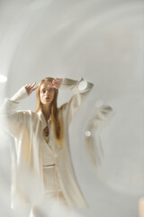Young woman in white outfit stands against white background, arms raised.