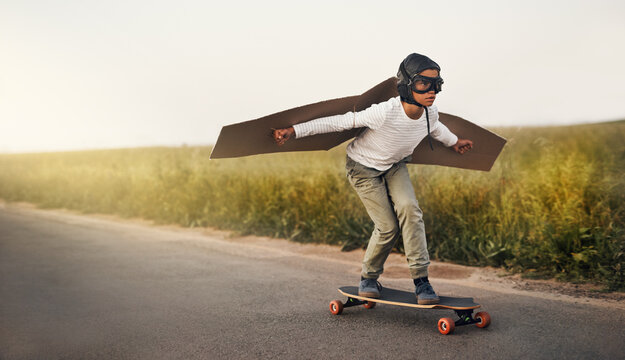 Skateboard, wings and child flying outdoor on road for airplane game, sport and holiday. Pilot, freedom and kid in helmet on street for childhood dream, fantasy and playing pretend for adventure