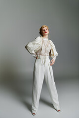 A stylish young woman wearing a white blouse and wide-leg trousers poses for a photograph.