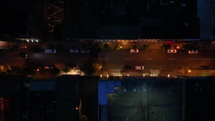 Driving cars on main street of small town at night. American housing area with warm lighting streetlights. Aerial top down tracking shot.