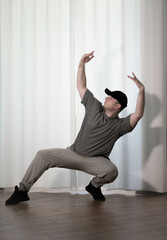 Dance in motion, pose of a man in hip-hop style clothes. Sports dancing guy in training poses. Dance training at home.