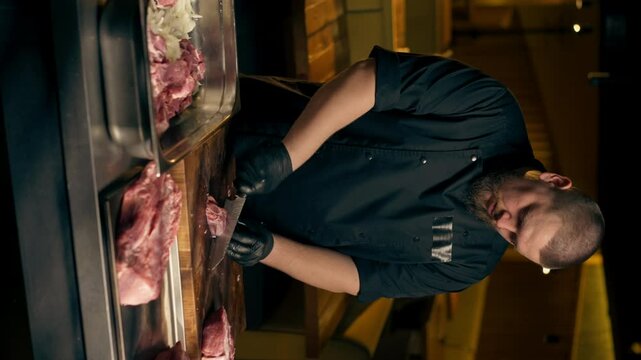 vertical video in a restaurant in a rib bar in the central hall, a chef in black gloves cuts large piece of pork meat into square pieces