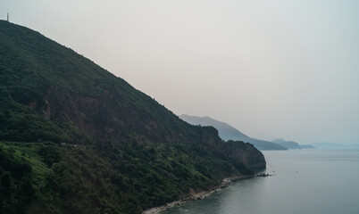 Coastal view of Budva, Montenegro. Green island, rocky mountain, clear sea, stone wall. Serene landscape