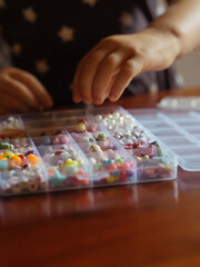 Kid Craft with Beads: A vertical close-up shot captures a toddler girl’s hands creating bead jewelry.