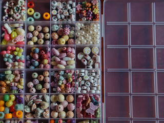 Kids Bead Set: A horizontal, straight-from-above close-up shot captures beads in a plastic box, divided into sections based on their shapes, colors, and forms.
