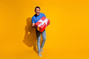 Full length photo of handsome young guy hold big present dressed stylish blue garment isolated on yellow color background