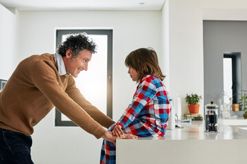 Obraz premium Dad, boy and kitchen for conversation in home, smile and love for discussion with child. Coffee, morning and pajamas for breakfast and talking with father person, cooking or bonding for nutrition