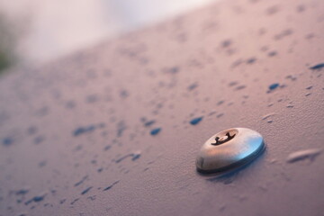 Macro of shiny metal bolt screwed in a plastic dark blue board with raindrops on it, well lit