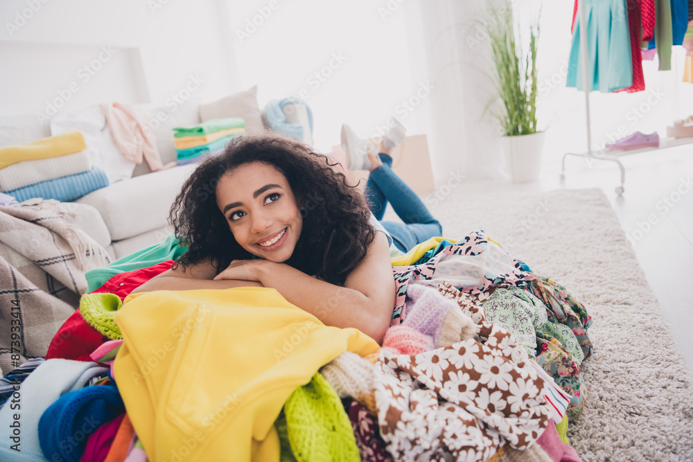 Wall mural full size photo of pretty young woman lying messy pile stack clothes fantasize apartment indoors