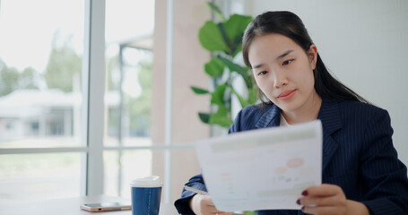 Portrait of Asian businesswoman in suit drink coffee while analyze documents and taking notes in small coffee shop. Work from anywhere, Remote working