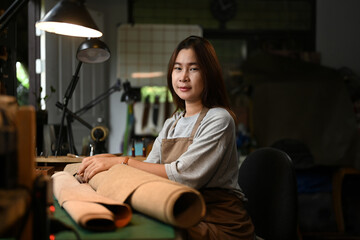 Portrait of a smiling craftswoman wearing an apron working on leather fabric at her workshop