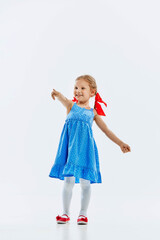 Little beautiful girl, child in cute blue dress pointing somewhere with cheerful smile isolated on white background. Curiosity in childhood. Concept of childhood, retro fashion, emotions, education