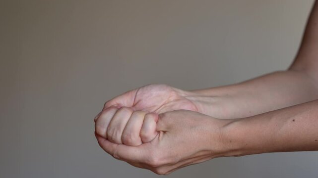 Young woman flexing fingers in her hand on a beige background. Numbness of the limbs. Injuries, Pain in the joints of the hands, carpal tunnel syndrome, neuralgia. Osteoarthritis, arthritis, bursitis