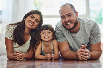 Obraz premium Parents, girl and happy in home on floor on portrait for fun, bonding and support for child development. People, couple and smile with kid or daughter in living room for love, relax and memories