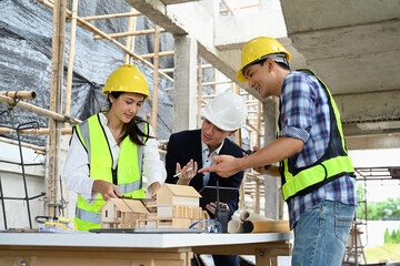 Engineers and businessman examining blueprints at table with architectural models in the foreground